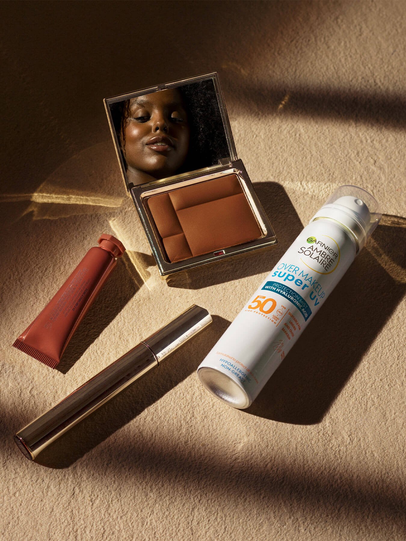 makeup mirror with model in reflection next to Ambre Solaire Super UV over makeup mist